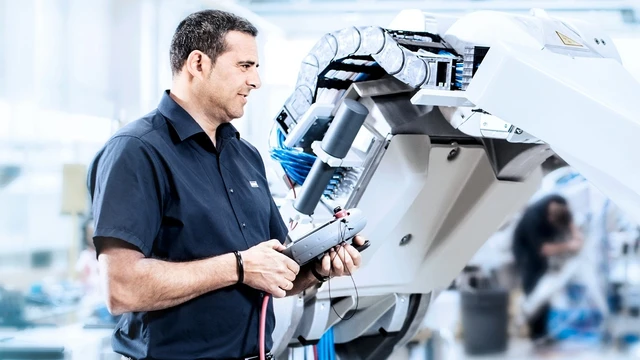 Engineer operating an industrial robot arm with a control device in a factory setting.