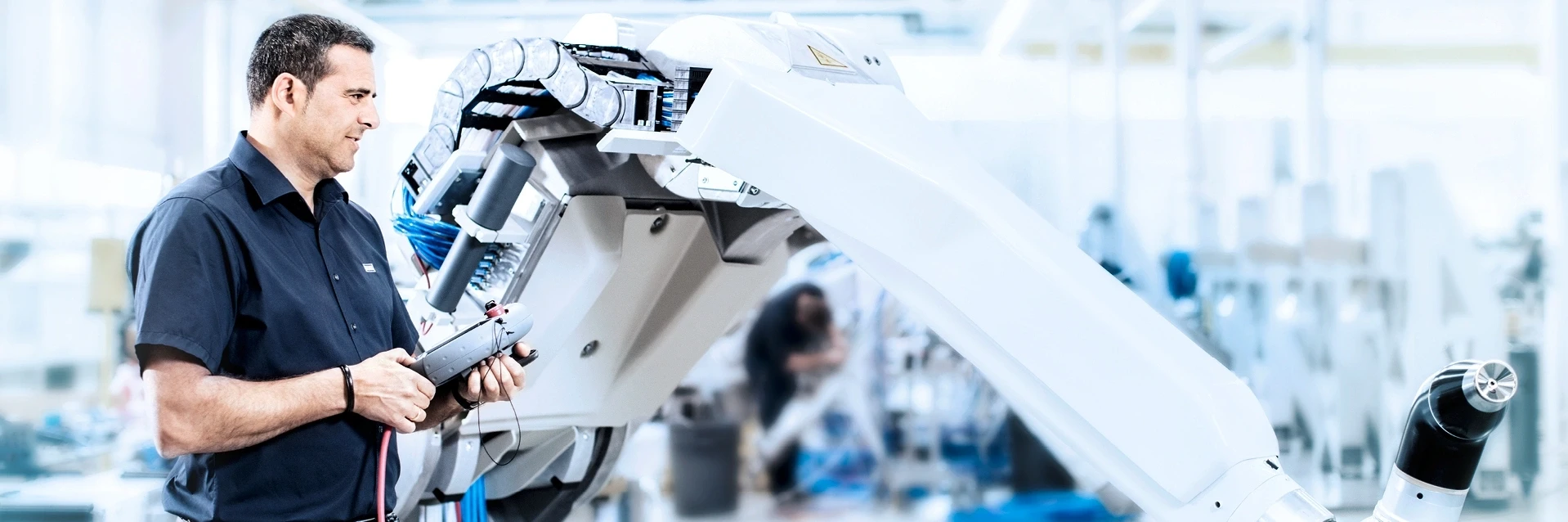 Engineer operating an industrial robot arm with a control device in a factory setting.
