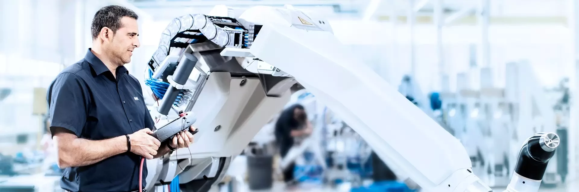 Engineer operating an industrial robot arm with a control device in a factory setting.