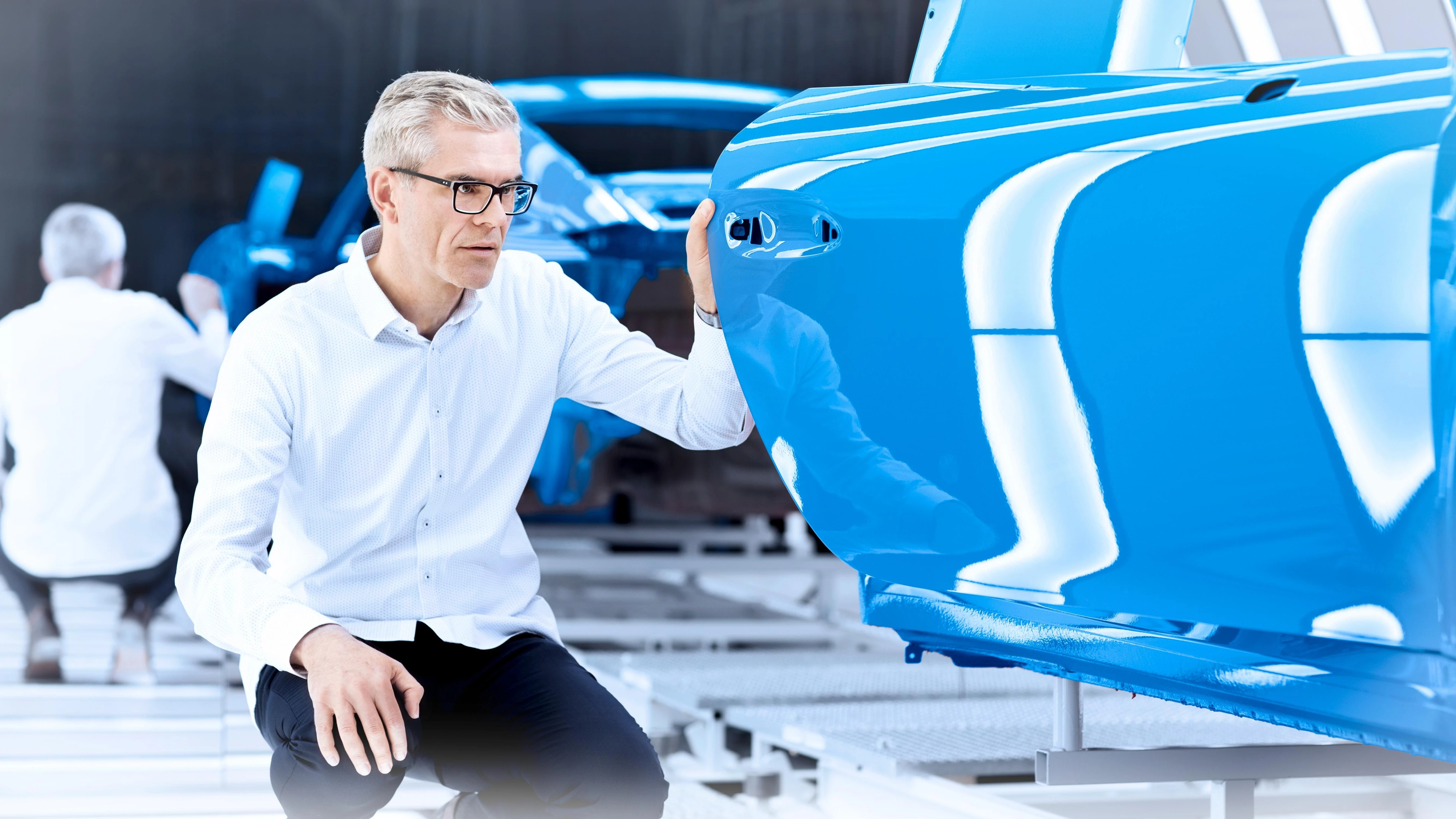 Employee inspecting a freshly painted blue car door in a modern automotive production facility.