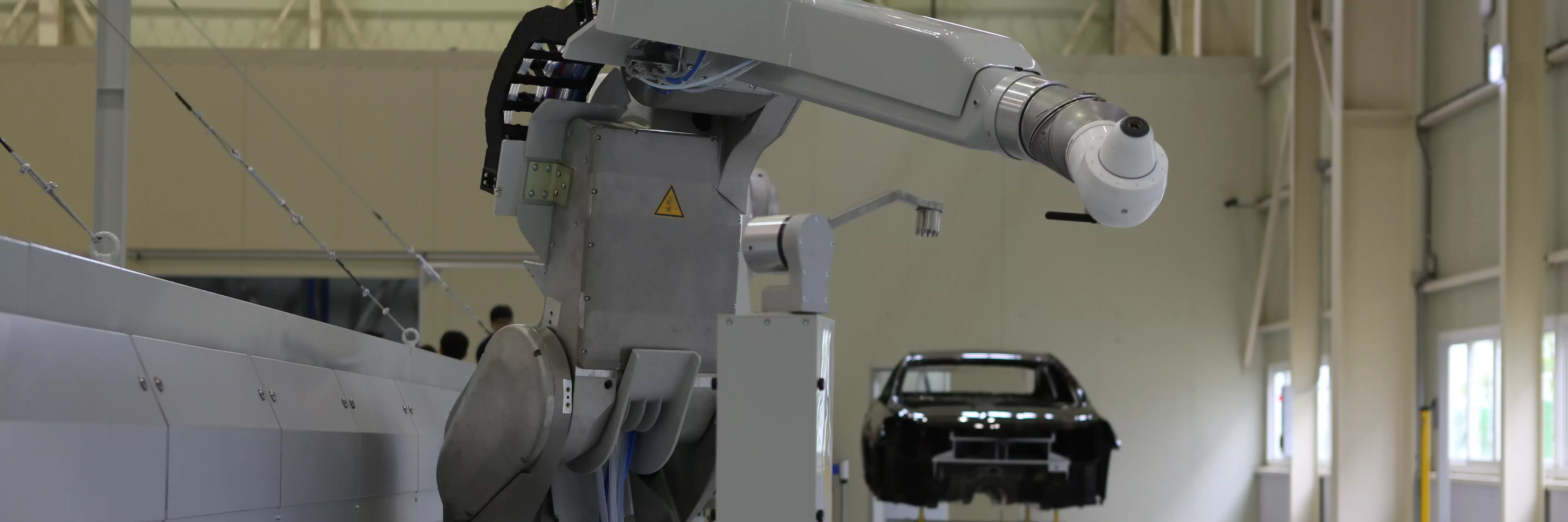 Industrial robot arm in a training facility in Korea, positioned near a car body shell on a stand.